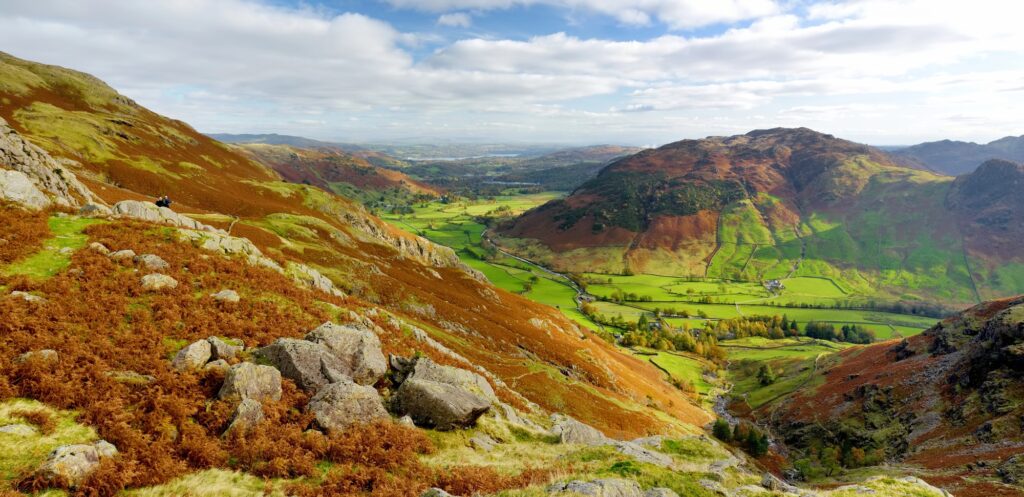 Felsiger Hang mit herbstlichem Farn über einem grünen Tal und Hügeln im Lake District