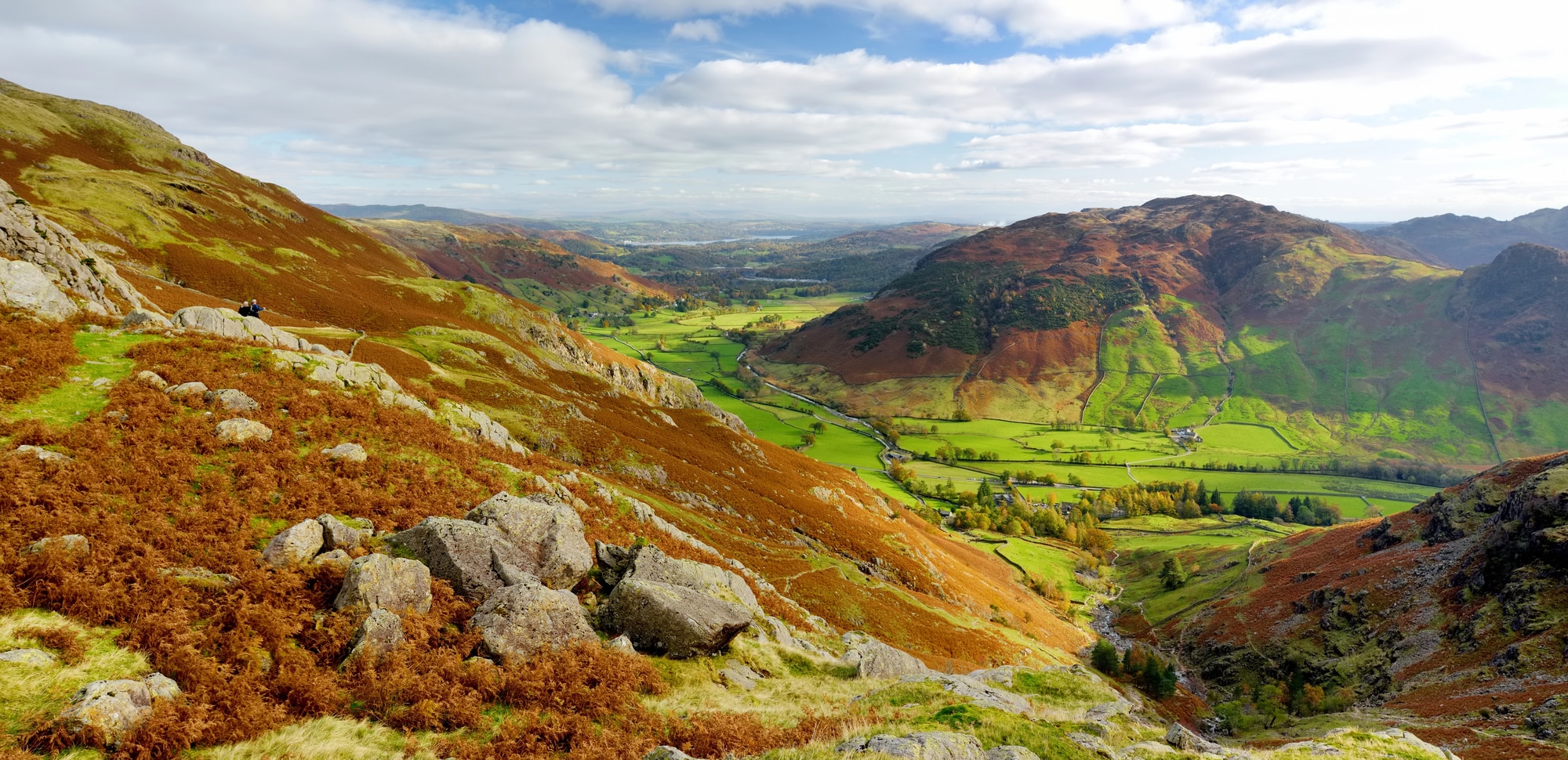 Felsiger Hang mit herbstlichem Farn über einem grünen Tal und Hügeln im Lake District
