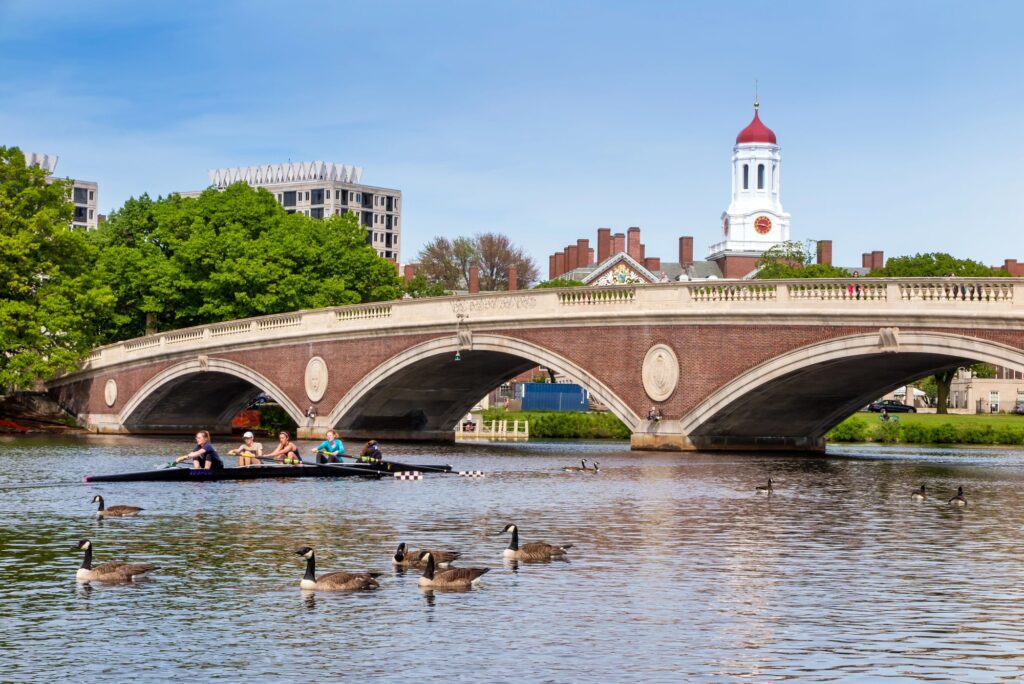 Backsteinbrücke mit Bögen über den Charles River, dahinter Bäume und ein Turm in Cambridge