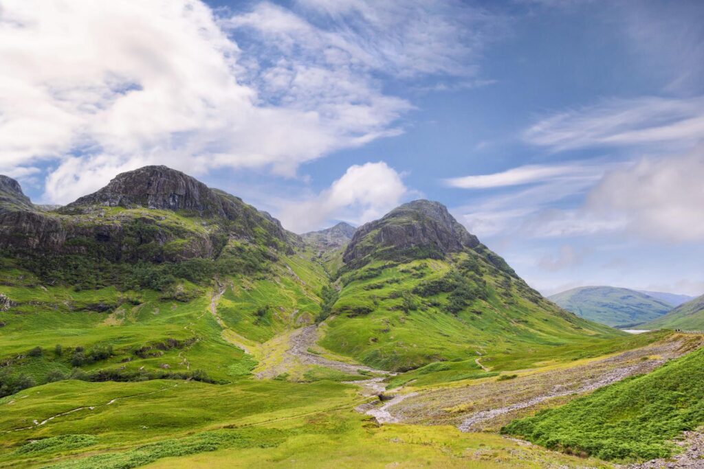 Grüne Berghänge und eine Straße im Tal unterhalb der Three Sisters von Glencoe