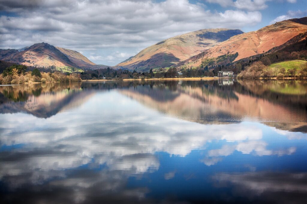 Herbstliche Hügel und Wolken spiegeln sich im ruhigen Wasser des Grasmere