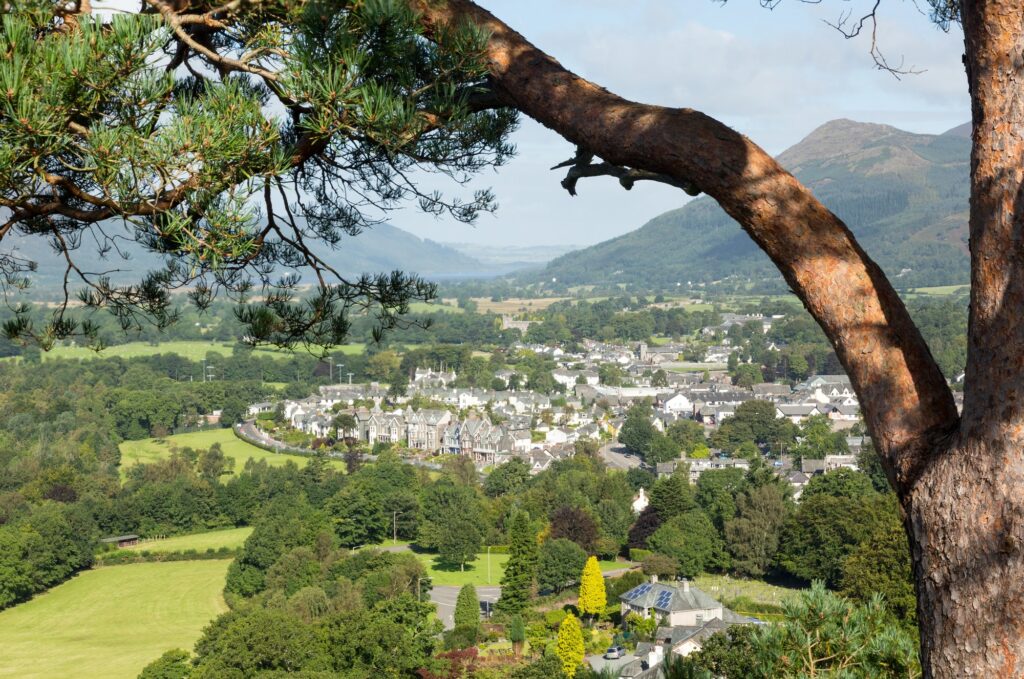 Blick von einem bewaldeten Hang auf Keswick mit grünen Feldern und Bergen dahinter
