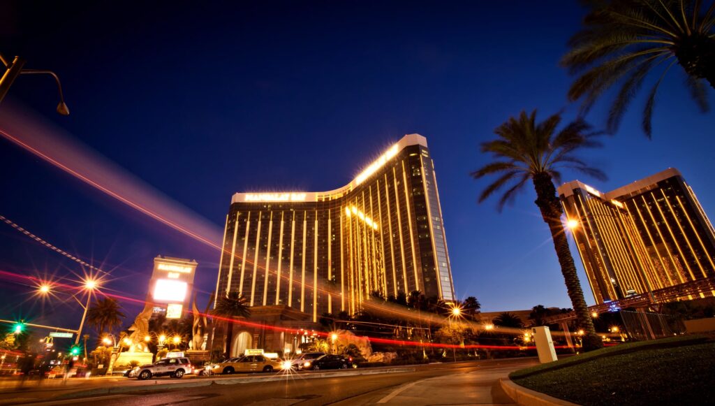 Beleuchteter Hotelturm des Mandalay Bay mit Palmen und vorbeifahrenden Autos bei Nacht