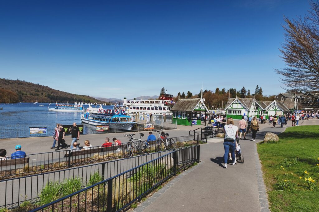 Spaziergänger an der Uferpromenade von Bowness-on-Windermere mit einem Boot auf dem See