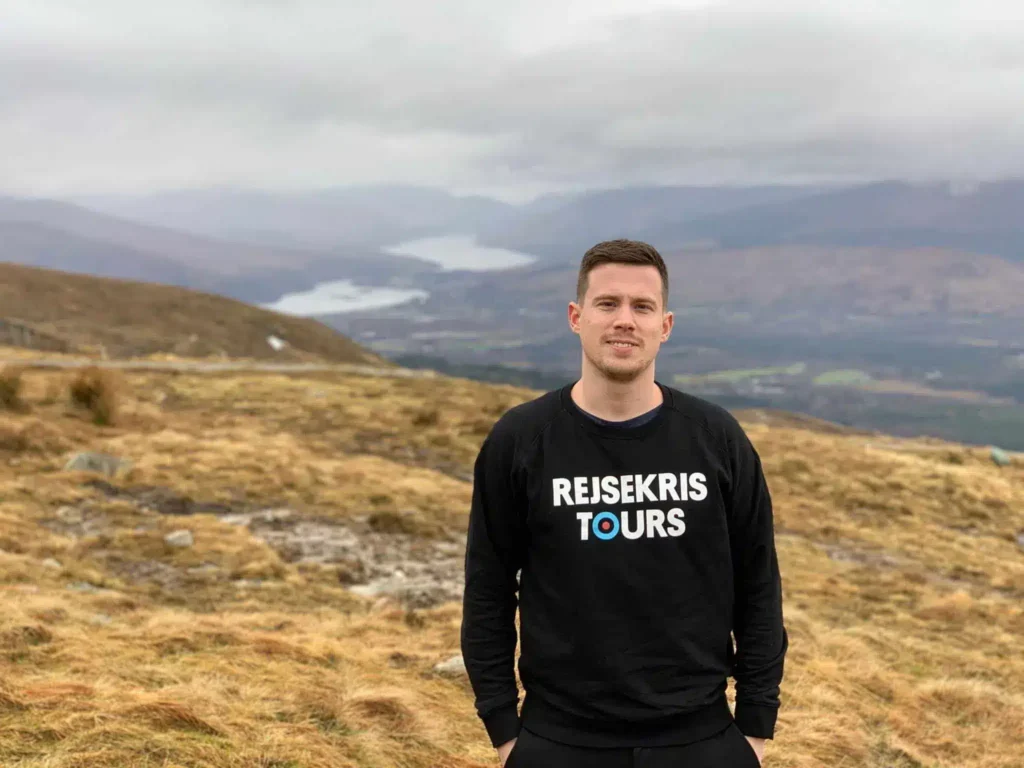 Ein Wanderer auf einem grasbewachsenen Hang mit Bergen in der Ferne bei Fort William