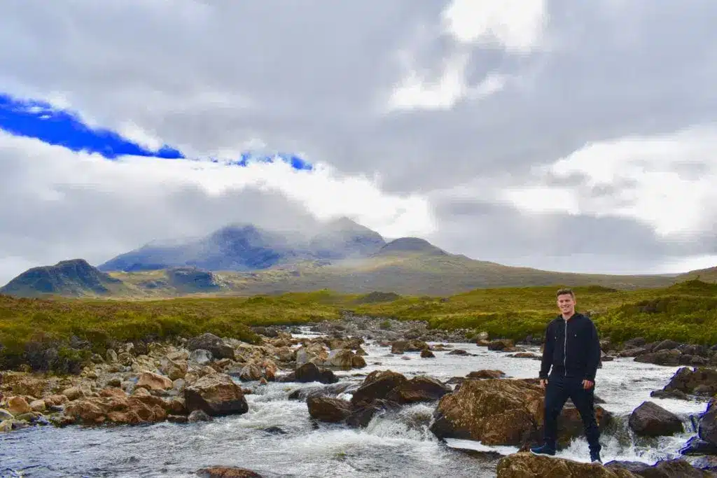 Ein Wanderer an einem felsigen Bach mit Bergen im Hintergrund auf der Isle of Skye