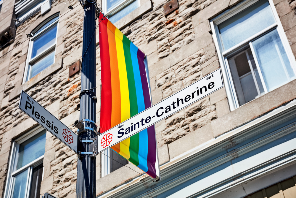 Straßenschilder der Rue Sainte-Catherine und der Rue Plessis mit Regenbogenflagge in The Village in Montreal