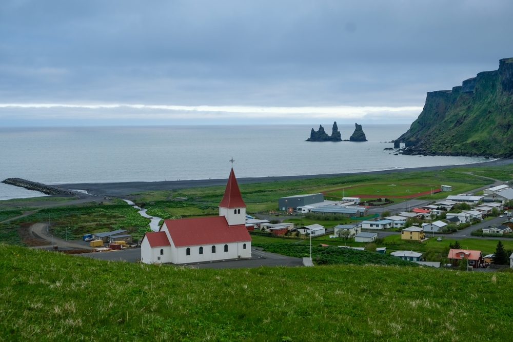 Vík mit der Kirche, dem schwarzen Strand und den Felsen Reynisdrangar an der Südküste Islands