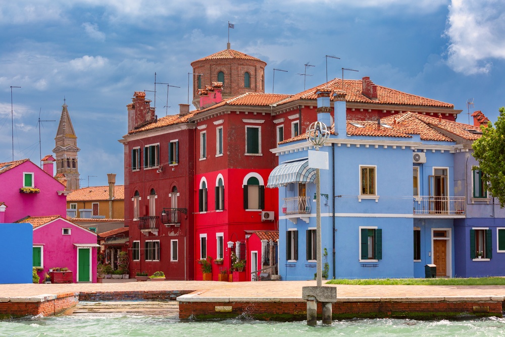Bunte Häuser an einem Kanal auf Burano mit dem Kirchturm im Hintergrund