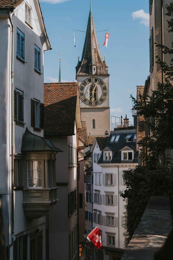 Gasse im Niederdorf in Zürich mit Schweizer Fahnen und dem Turm von St. Peter im Hintergrund