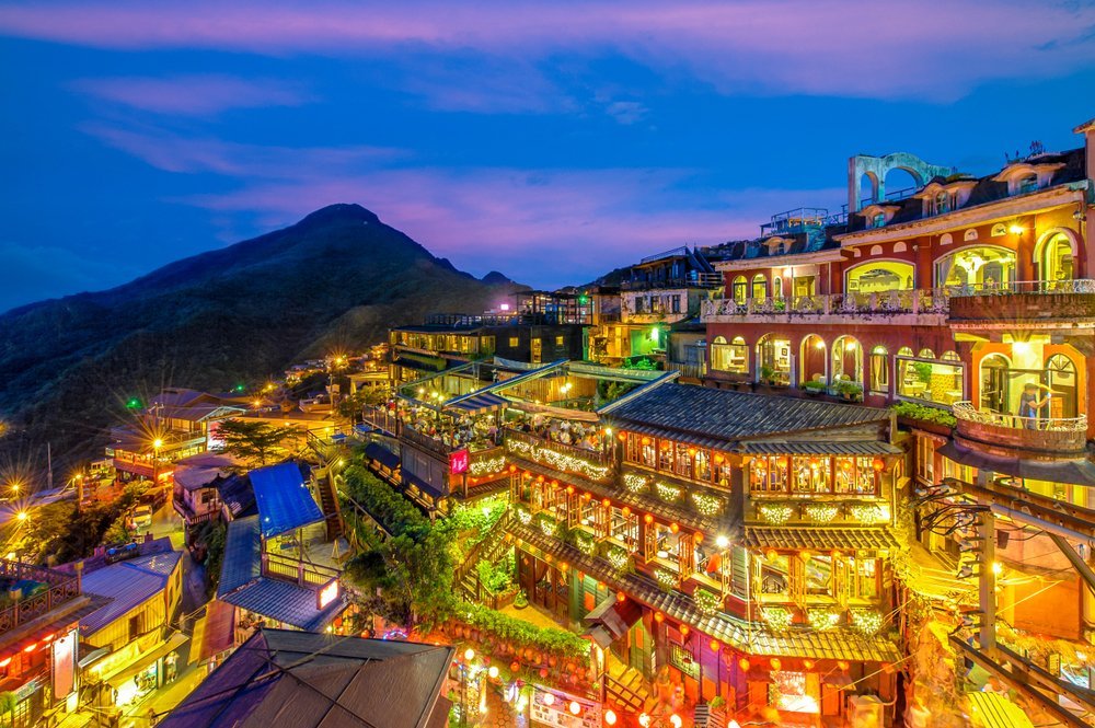 Jiufen am Abend mit beleuchteten Häusern und Teehäusern am Berghang über dem Meer