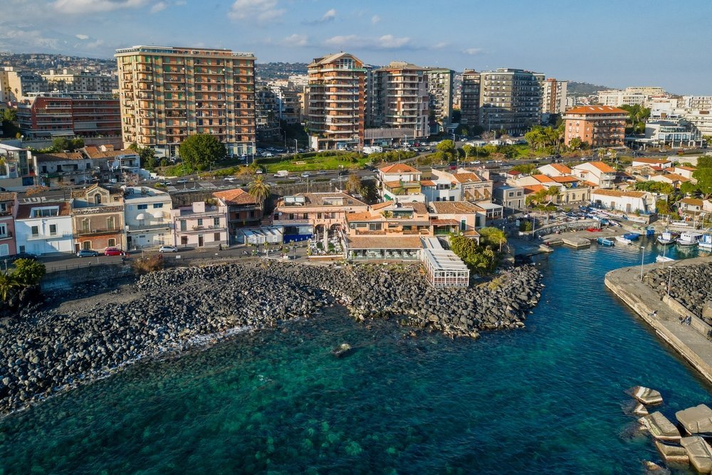 Der kleine Hafen und der schwarze Lavastrand von San Giovanni li Cuti in Catania