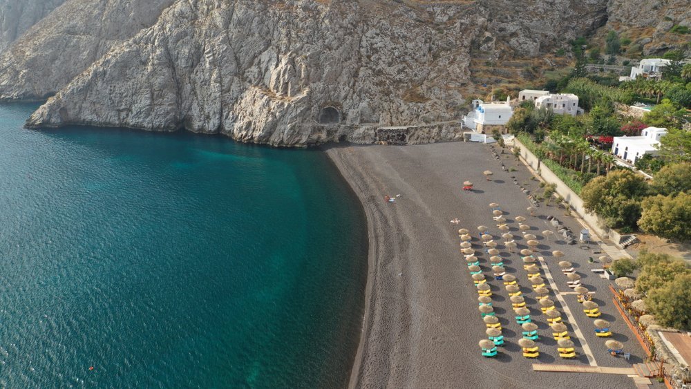 Der Ort Kamari und der Strand mit Sonnenliegen aus der Luft