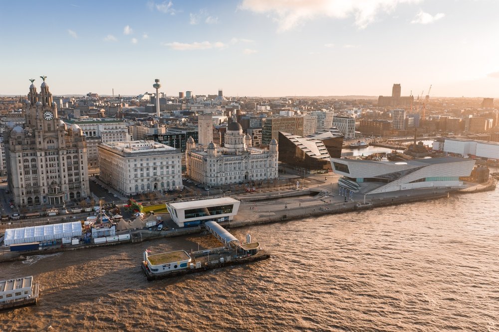 Luftaufnahme der Liverpooler Hafenpromenade mit den Three Graces und der Kathedrale bei Sonnenaufgang