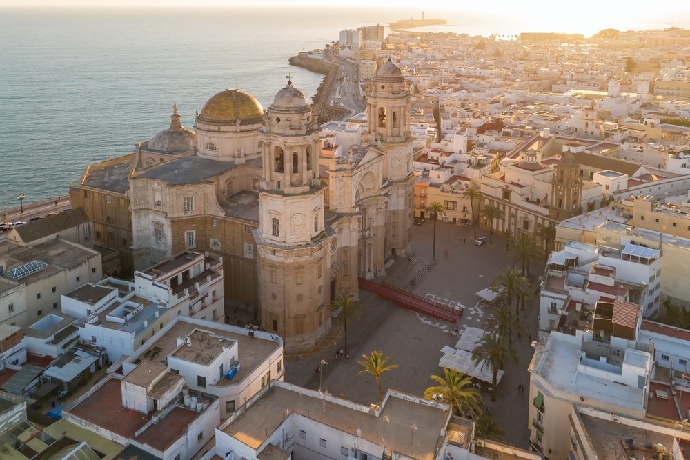Luftaufnahme der Kathedrale und der Altstadt von Cádiz bei Sonnenuntergang, dahinter der Atlantik